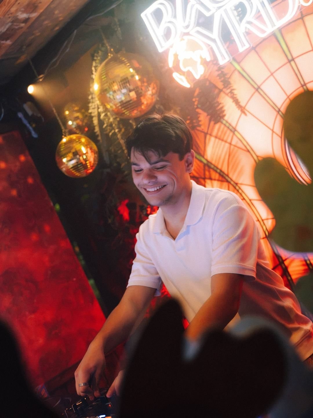 DJ laughing behind the decks under the BaseYRD neon sign at LouLou, Eindhoven